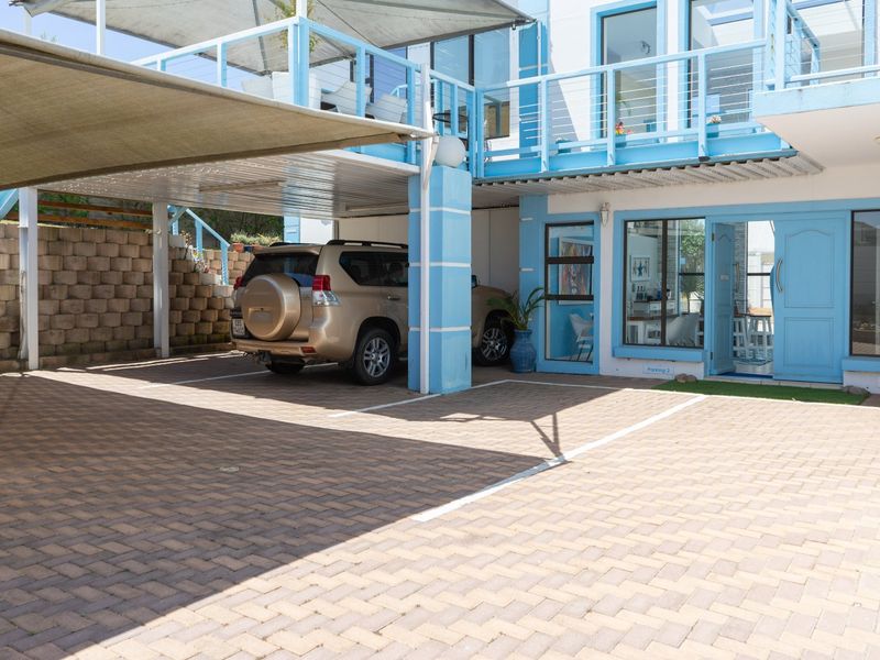 Front exterior view featuring a paved driveway, covered carport with shade sail, and a multi-level building facade with balcony access.