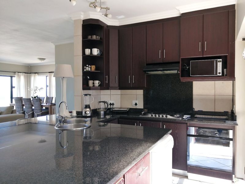 Open-plan kitchen featuring dark wood cabinetry, granite countertops, built-in oven, gas hob, and an integrated microwave, flowing into the adjacent living and dining area.