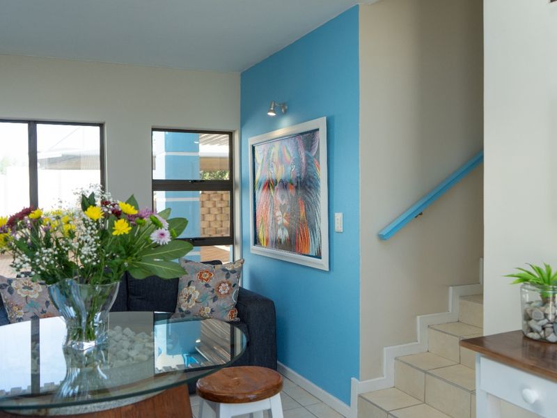 A bright living area featuring tiled flooring, a staircase with a blue handrail, and large windows allowing for natural light.
