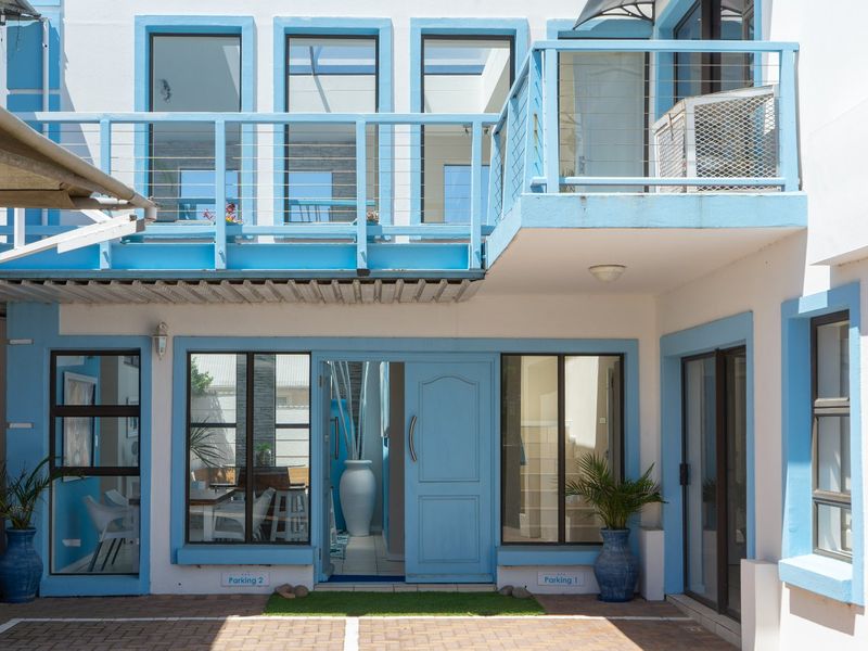 Front facade of a multi-level property featuring a paved driveway, blue-trimmed windows and doors, and an upper-level balcony with metal railings.
