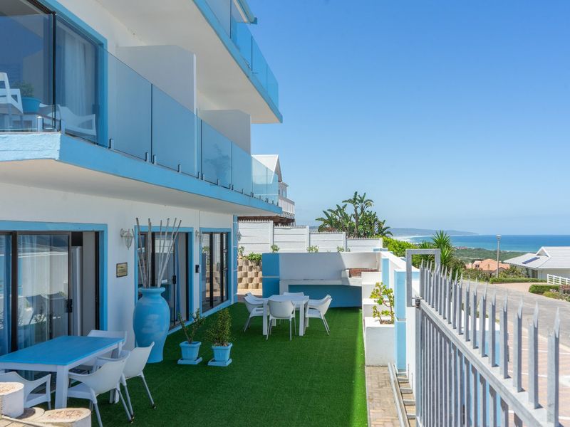Spacious outdoor patio area featuring a built-in braai, glass balustrades, and direct access to the living area with scenic coastal views.