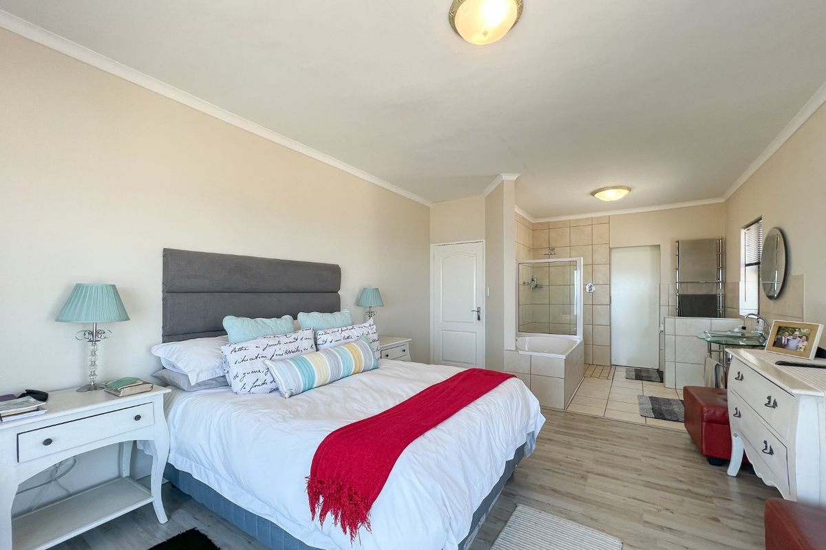 Spacious bedroom featuring light laminate flooring and an open-plan en-suite bathroom with a glass shower enclosure and built-in bathtub.