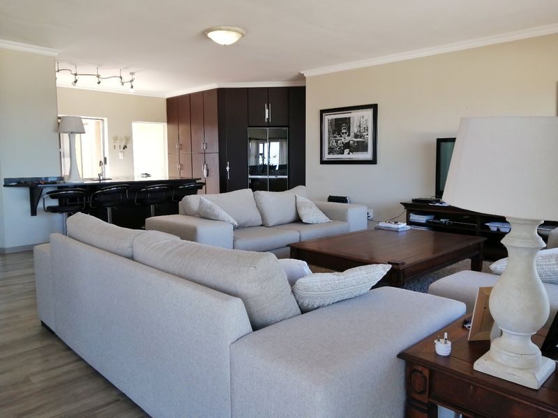 Spacious open-plan living area featuring a modern kitchen with dark cabinetry, a breakfast island, and light-toned laminate flooring throughout.
