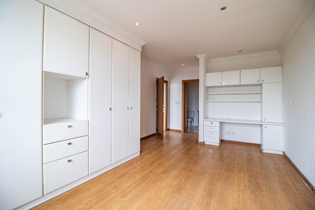 Spacious bedroom featuring extensive built-in cabinetry, a dedicated study desk area, and durable laminate flooring with neutral finishes.