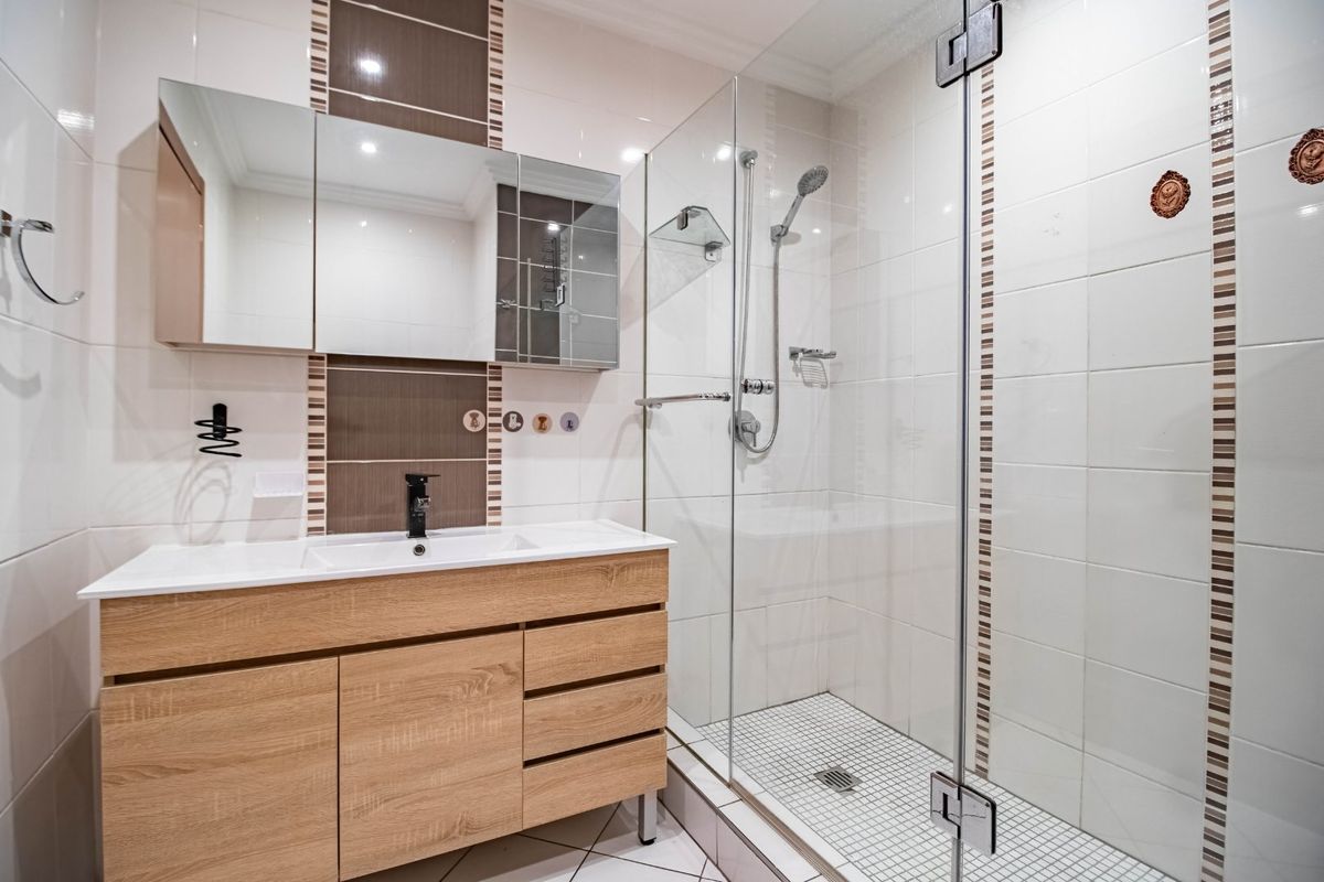 Modern bathroom featuring a wood-finish vanity cabinet, integrated sink, mirrored medicine cabinet, and a spacious walk-in shower with glass enclosure.