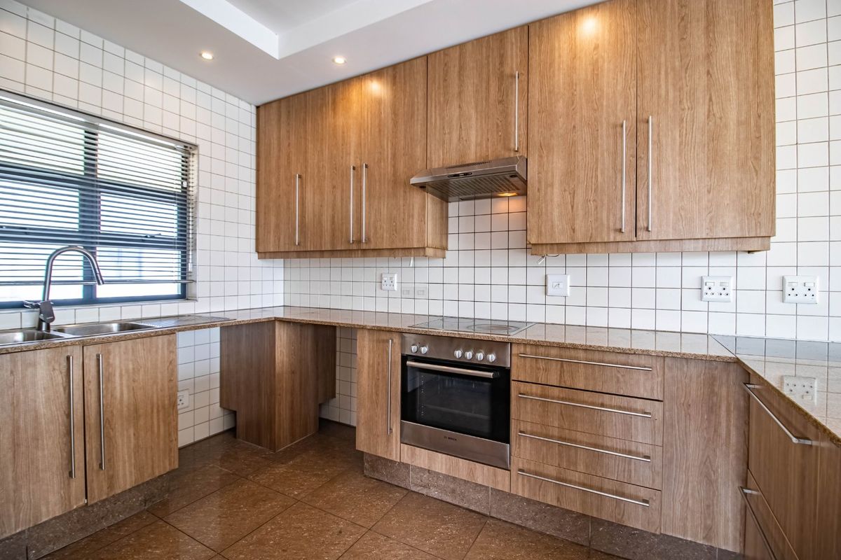 Modern kitchen featuring wood-look cabinetry, granite countertops, stainless steel oven, electric hob, and a tiled backsplash in a clean, well-lit space.
