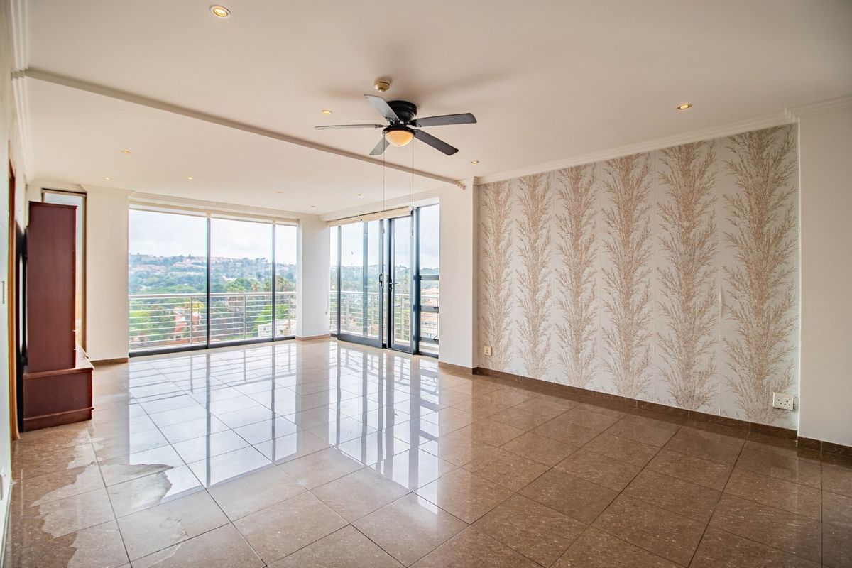 Spacious, empty living area featuring polished tile flooring, a ceiling fan, and large sliding glass doors leading to a balcony with scenic views.