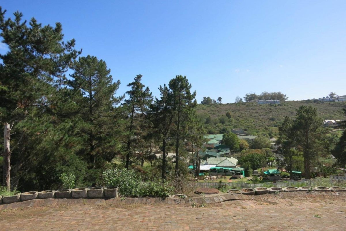 A scenic elevated view overlooking a green valley with mature trees and distant residential structures, featuring a brick-paved foreground.