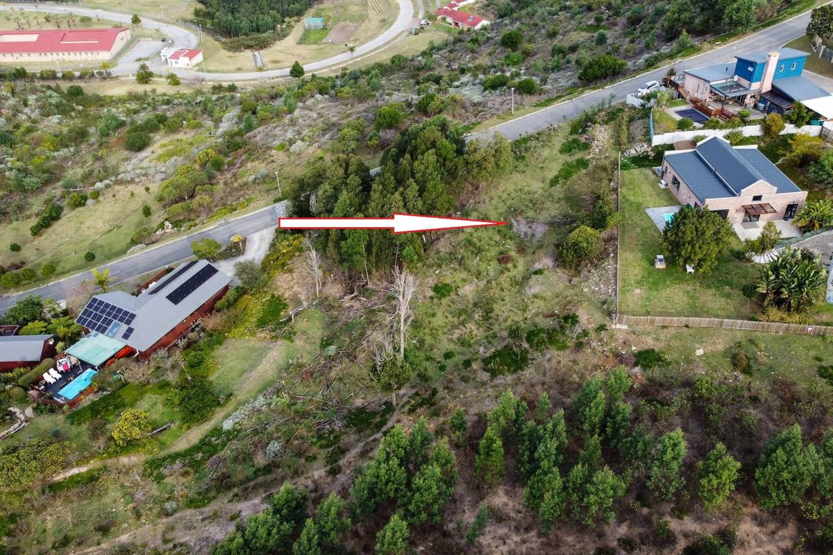An aerial view of a vacant residential plot featuring sloped terrain and natural vegetation, situated within an established neighborhood.