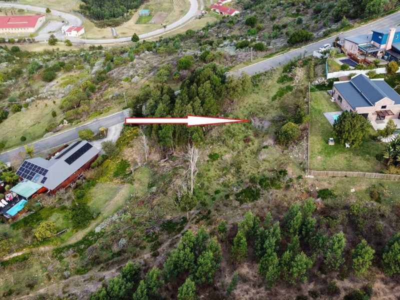 An aerial view of a vacant residential plot featuring sloped terrain and natural vegetation, situated within an established neighborhood.