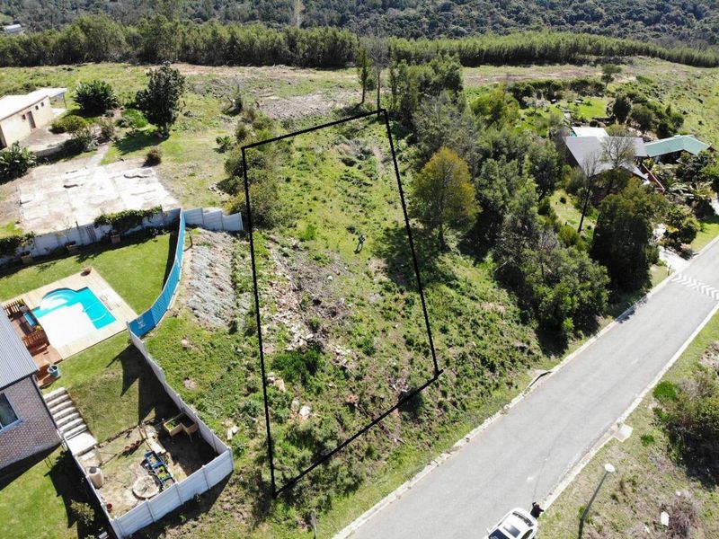 Aerial view of a vacant residential plot with sloped terrain, situated in a quiet neighborhood setting.