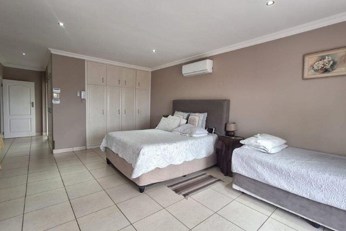 Spacious bedroom featuring neutral wall tones, tiled flooring, built-in cabinetry, and a wall-mounted air conditioning unit.
