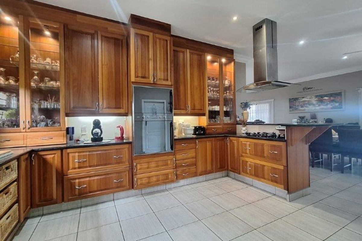 Spacious kitchen featuring warm-toned wooden cabinetry, granite countertops, built-in oven, gas hob, and a stainless steel extractor fan, seamlessly flowing into the dining area.
