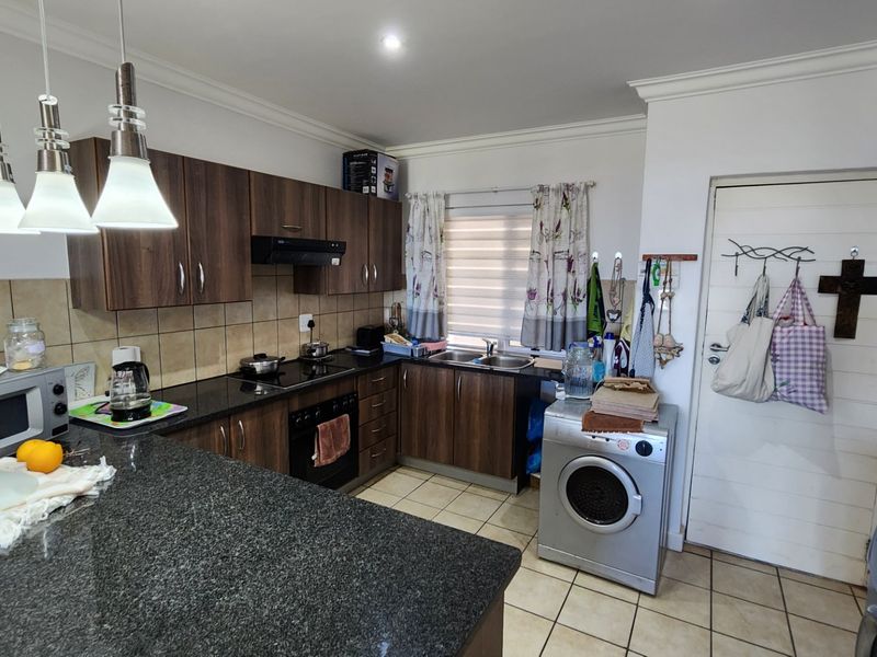 A functional kitchen featuring dark wood cabinetry, granite countertops, a built-in oven with hob, and tiled flooring with integrated laundry space.