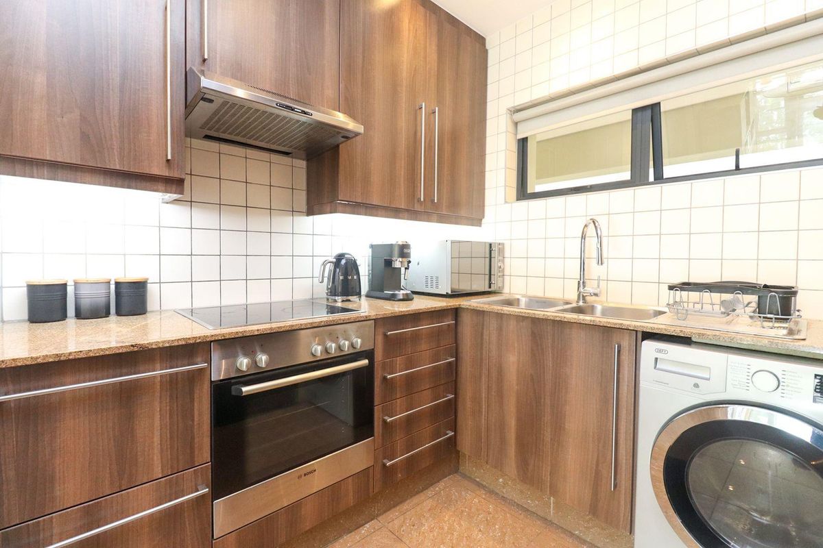 A functional kitchen featuring wood-veneer cabinetry, granite countertops, a built-in oven with electric hob, and integrated space for a washing machine.