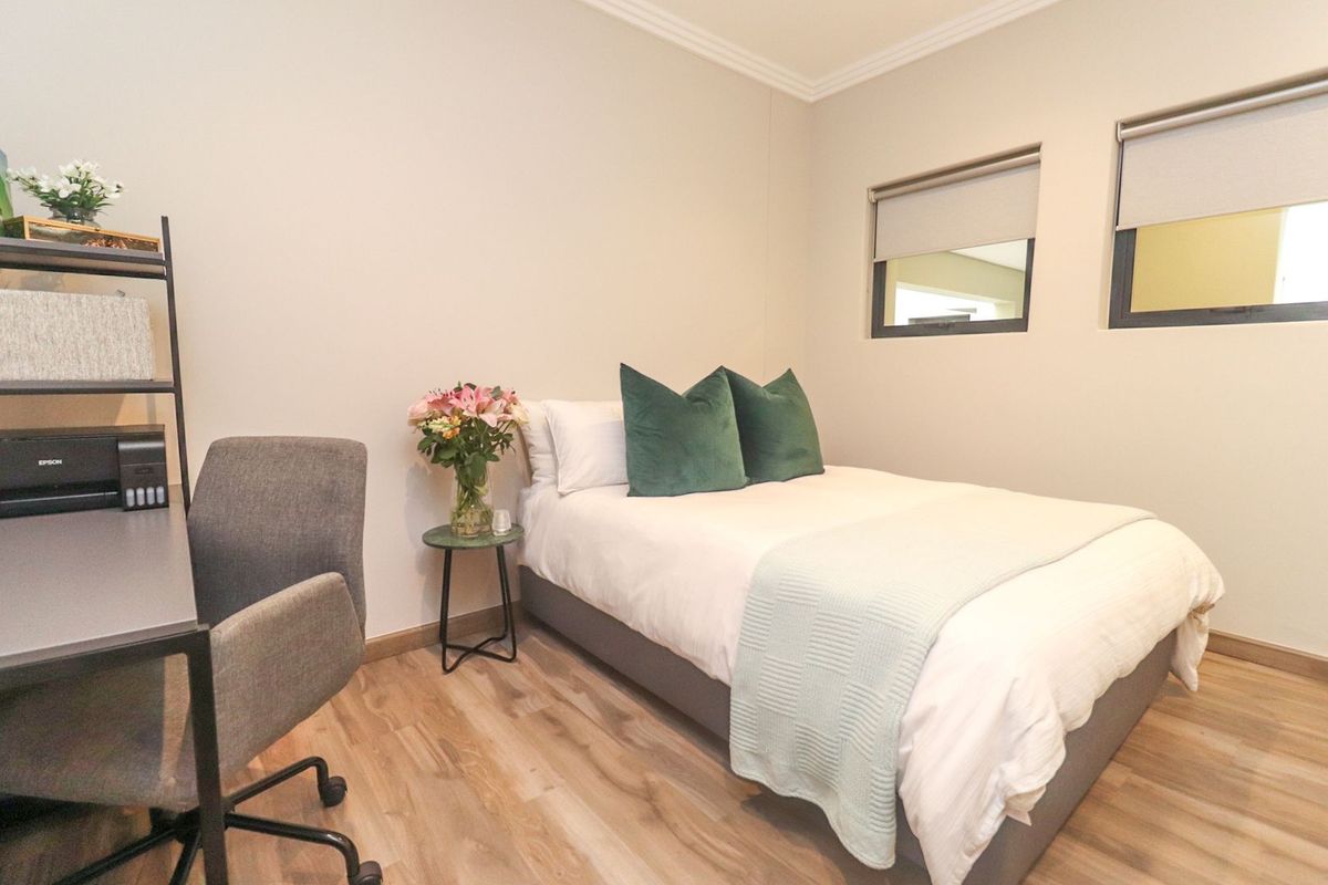 A well-maintained bedroom featuring light-toned laminate flooring, neutral walls, and dual windows fitted with modern roller blinds.