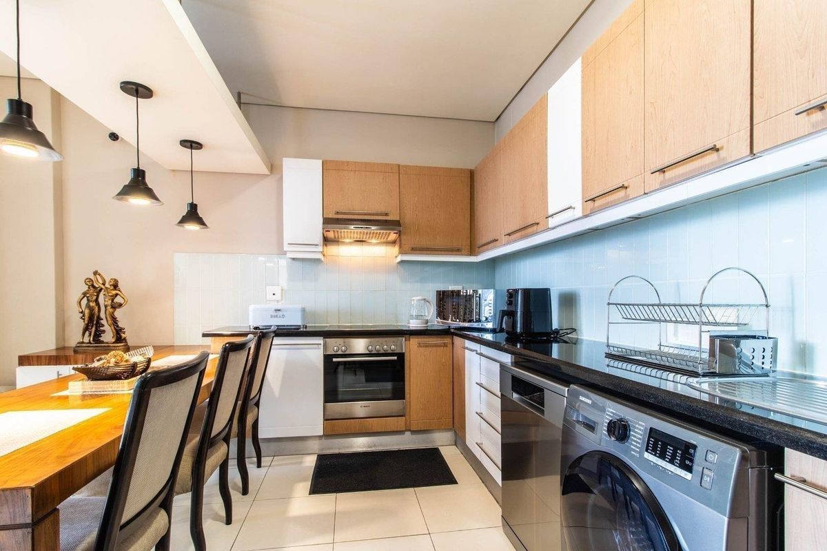 Modern kitchen featuring light wood and white cabinetry, black granite countertops, integrated oven, extractor fan, and stylish pendant lighting over the adjacent dining area.