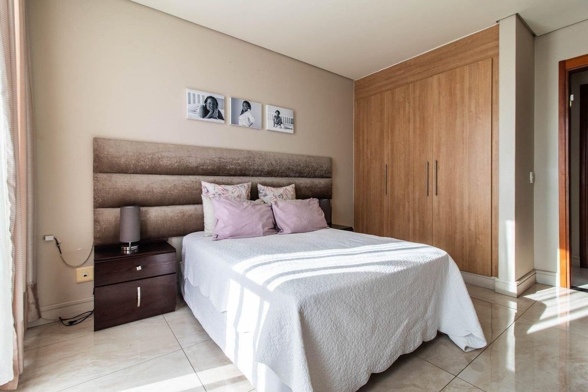 A well-maintained bedroom featuring neutral wall tones, large format floor tiles, and integrated wood-finish built-in wardrobes.