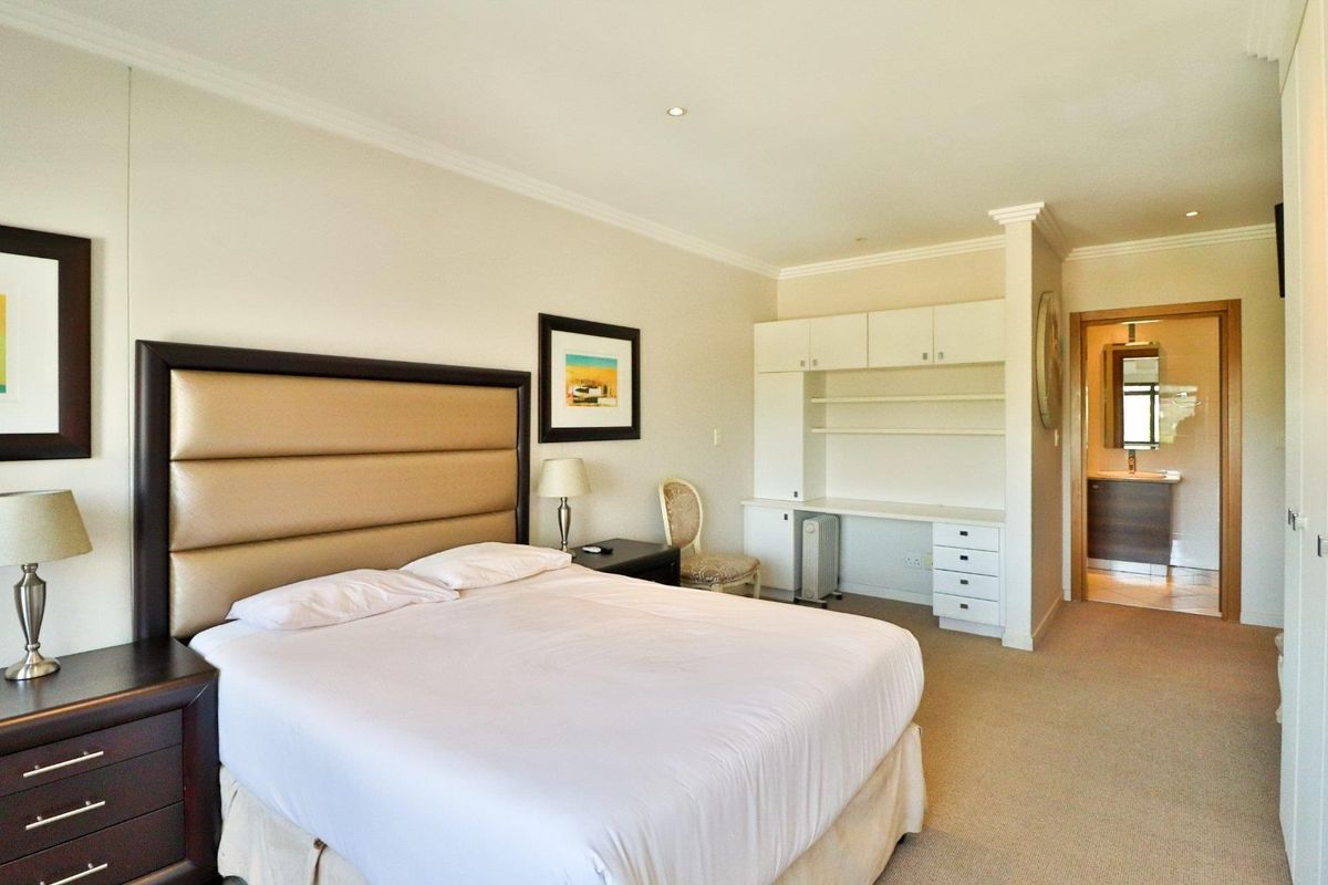 Spacious bedroom featuring neutral carpeting, built-in desk with overhead storage, and direct access to an en-suite bathroom.