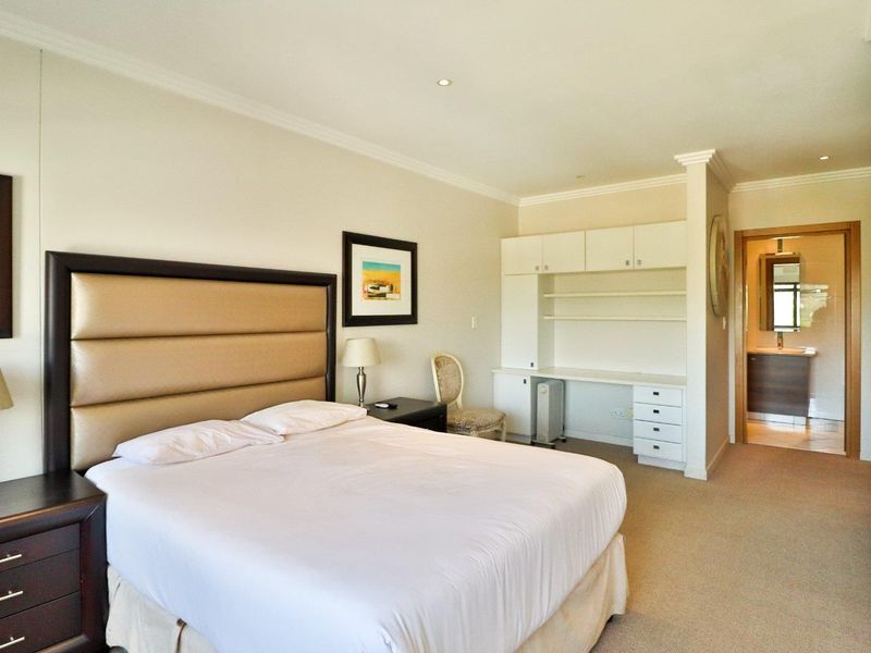 Spacious bedroom featuring neutral carpeting, built-in desk with overhead storage, and direct access to an en-suite bathroom.