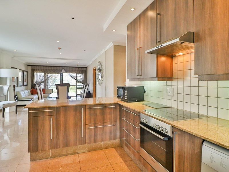 Open-plan kitchen featuring wood-finish cabinetry, granite countertops, and integrated appliances, flowing seamlessly into the adjacent living and dining area.