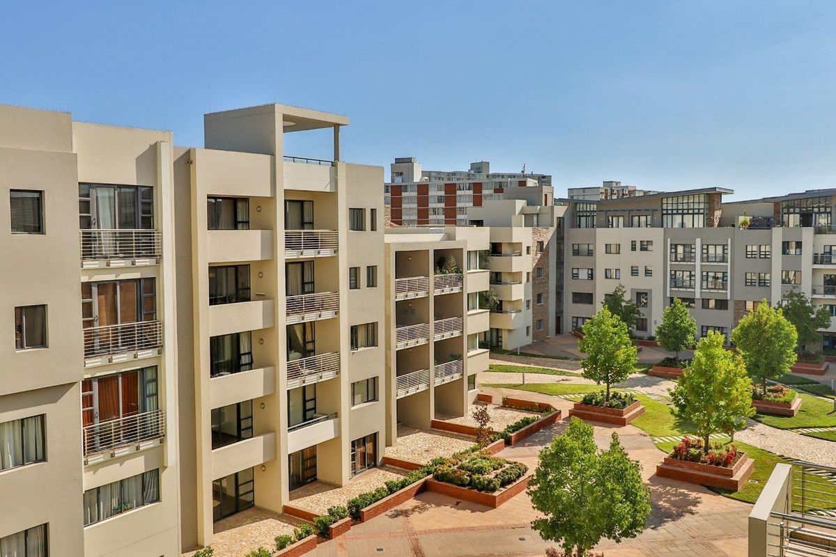 Elevated view of a modern apartment complex featuring multiple balconies, landscaped courtyards, and paved walkways between residential blocks.