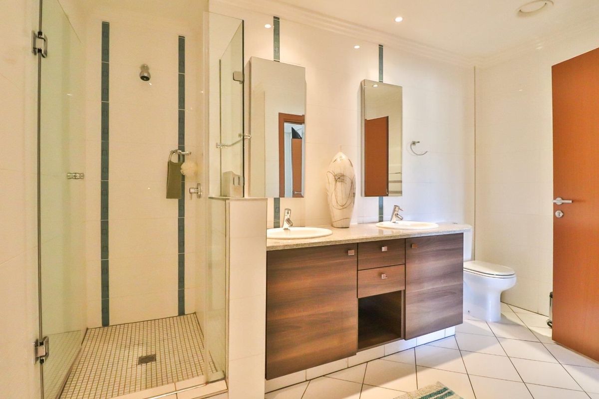 Modern bathroom featuring a double vanity with wood-finish cabinetry, a spacious walk-in shower with glass enclosure, and neutral floor tiling.