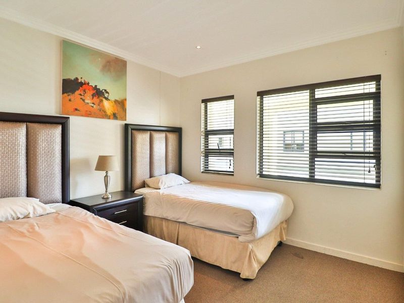 A well-maintained bedroom featuring neutral walls, carpeted flooring, built-in cupboards, and large windows with fitted venetian blinds for natural light control.