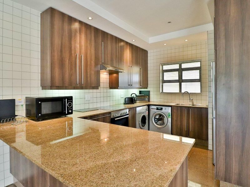 Modern kitchen featuring wood-finish cabinetry, granite countertops, integrated appliances, and a tiled backsplash, offering a functional and well-maintained cooking space.