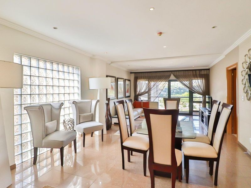 Spacious open-plan living and dining area featuring polished tile flooring, a decorative glass block wall, and sliding doors leading to a balcony.