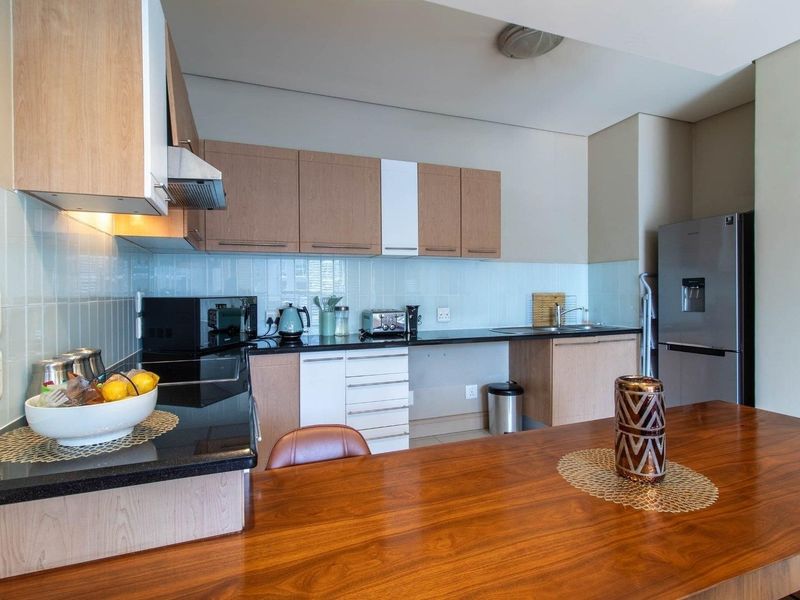 A functional kitchen featuring light wood cabinetry, black granite countertops, a tiled backsplash, and integrated appliances, offering a clean and practical cooking space.