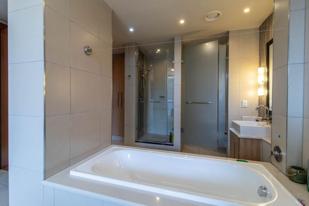 Modern bathroom featuring a built-in bathtub, separate glass-enclosed shower, vanity unit with basin, and neutral wall tiling with recessed lighting.