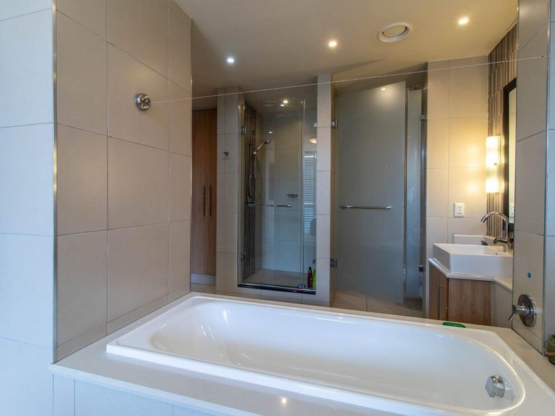 Modern bathroom featuring a built-in bathtub, separate glass-enclosed shower, vanity unit with basin, and neutral wall tiling with recessed lighting.