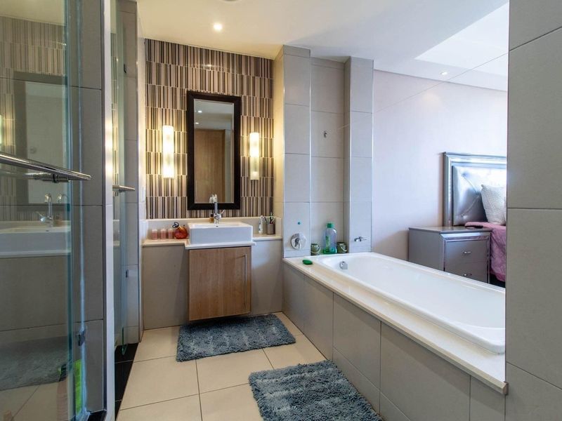 Modern bathroom featuring a vessel sink, vanity cabinet, built-in bathtub, and a glass-enclosed shower with contemporary tiled finishes.