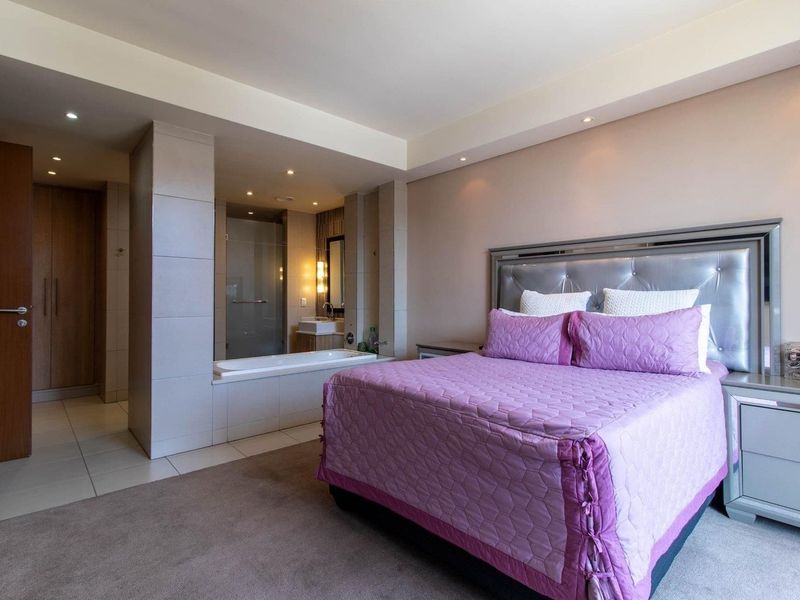 Spacious bedroom featuring an open-plan en-suite bathroom with a built-in bathtub, shower, and ample built-in cupboard storage.