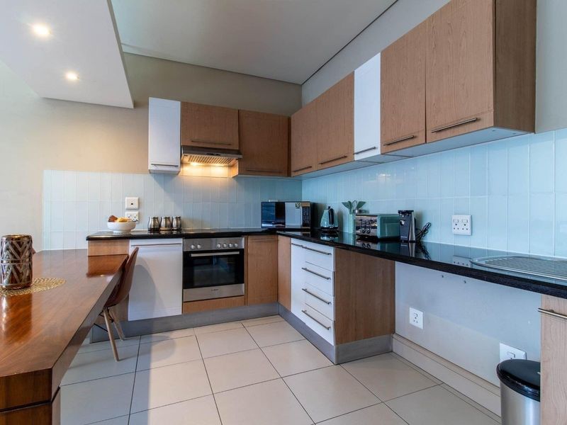 Modern kitchen featuring wood-tone cabinetry, black granite countertops, a tiled backsplash, and integrated appliances, offering a clean and functional cooking space.