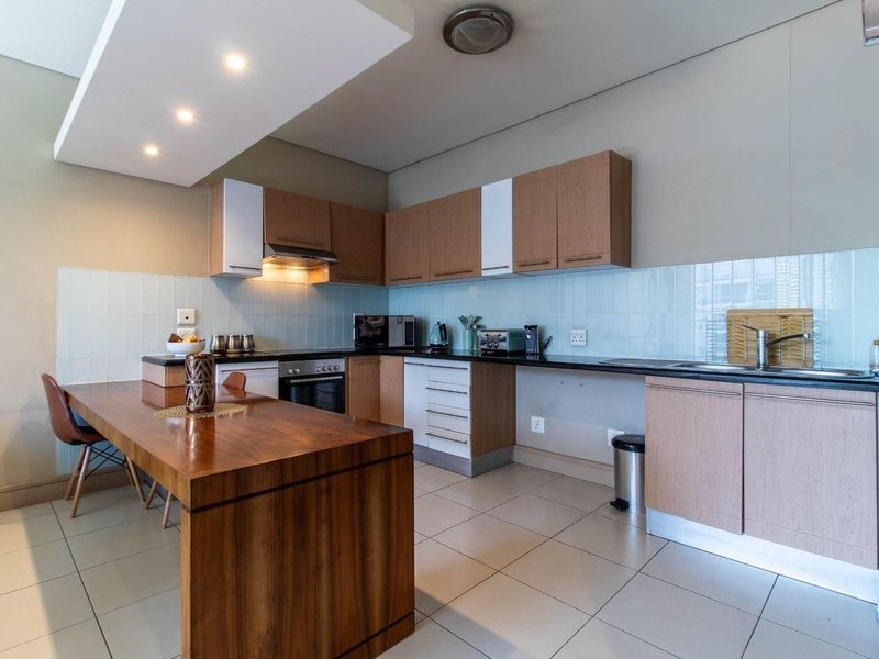 Modern kitchen featuring wood-finish cabinetry, dark countertops, integrated appliances, a tiled backsplash, and a functional breakfast bar island.