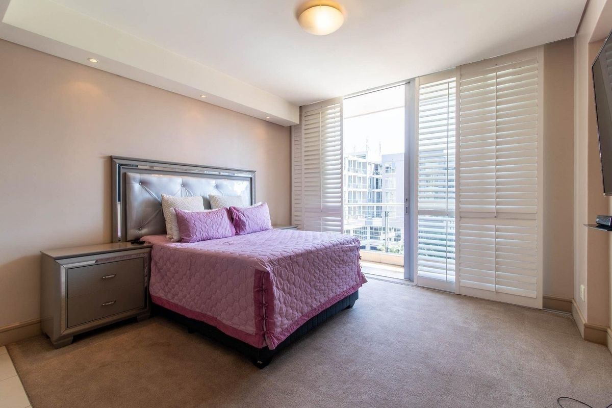 A well-maintained bedroom featuring neutral carpeting, recessed lighting, and plantation shutters opening onto a private balcony.