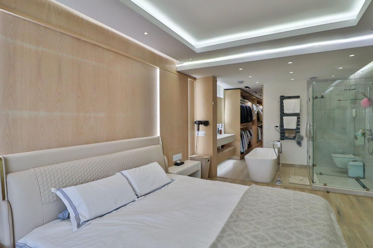 Luxurious master bedroom suite featuring integrated walk-in closet, open-plan bathroom with freestanding tub, glass shower, and sophisticated wood-paneled accent wall with ambient lighting.
