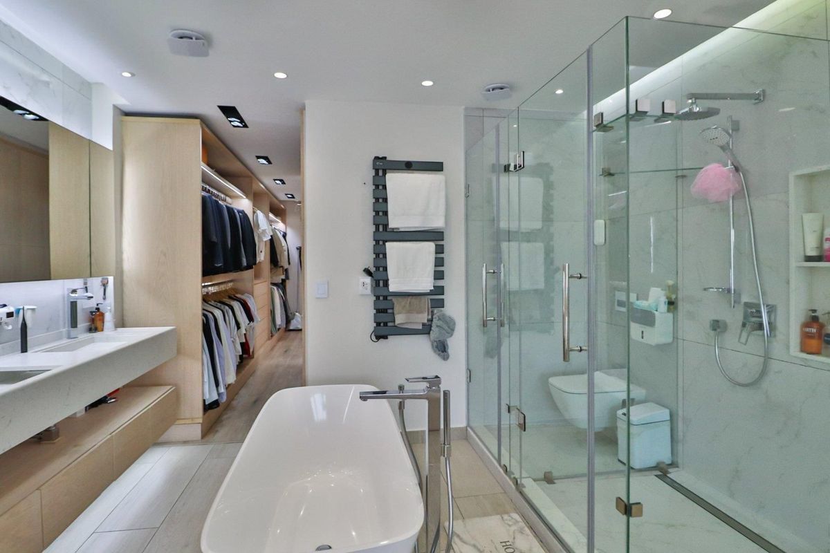 Modern luxury bathroom featuring a freestanding bathtub, walk-in glass shower, wall-mounted toilet, and integrated walk-in closet with custom cabinetry.