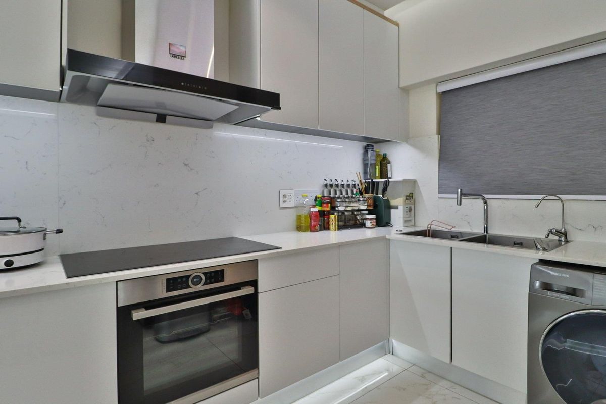 Modern kitchen featuring sleek handleless cabinetry, stone countertops, marble-look backsplash, integrated oven, induction hob, and a double sink with under-cabinet lighting.
