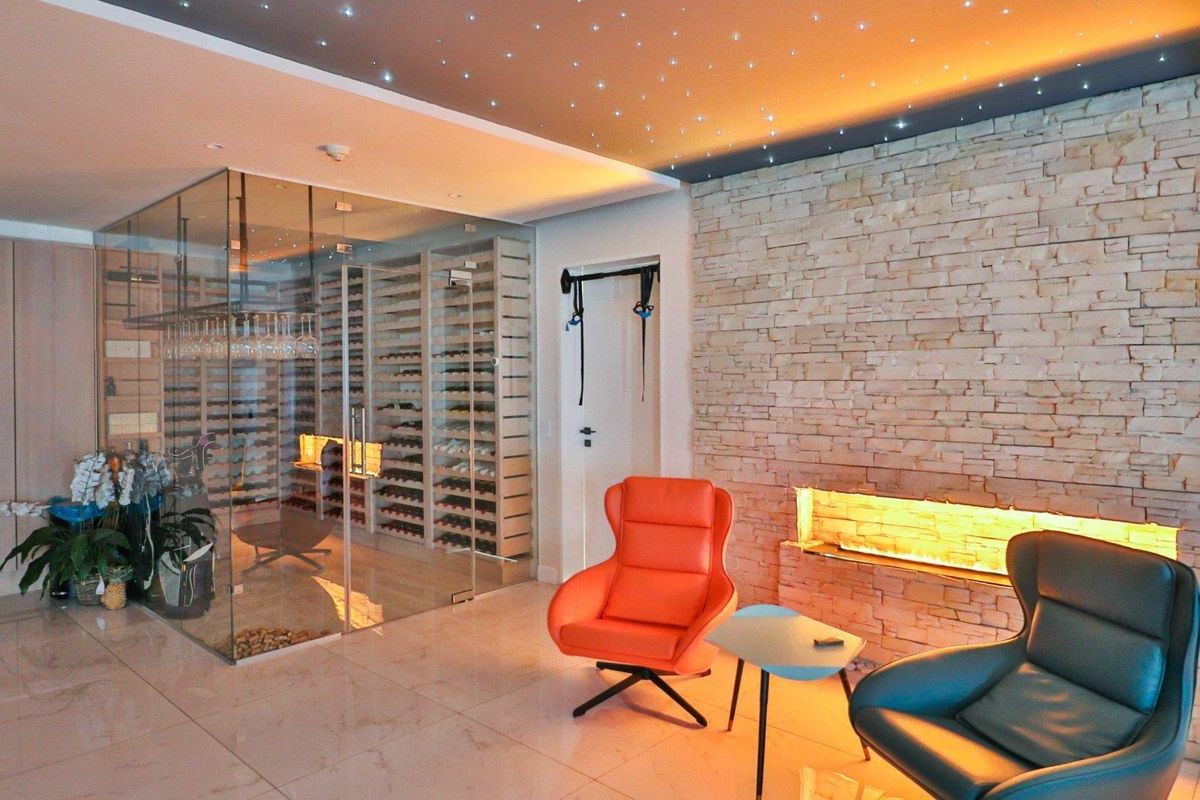 A sophisticated lounge area featuring a glass-enclosed wine cellar, a textured stone feature wall with a built-in fireplace, and a decorative starlight ceiling.