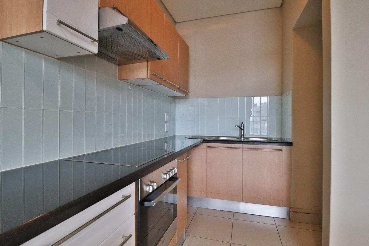 A clean, functional kitchen featuring light wood cabinetry, dark countertops, a tiled backsplash, and integrated appliances including an oven and cooktop.