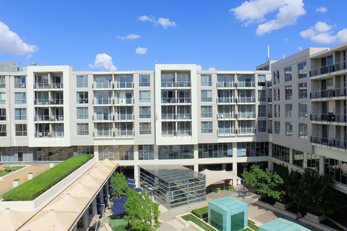 An elevated view of a modern apartment complex featuring a central landscaped courtyard, glass atrium, and multiple levels of private balconies.