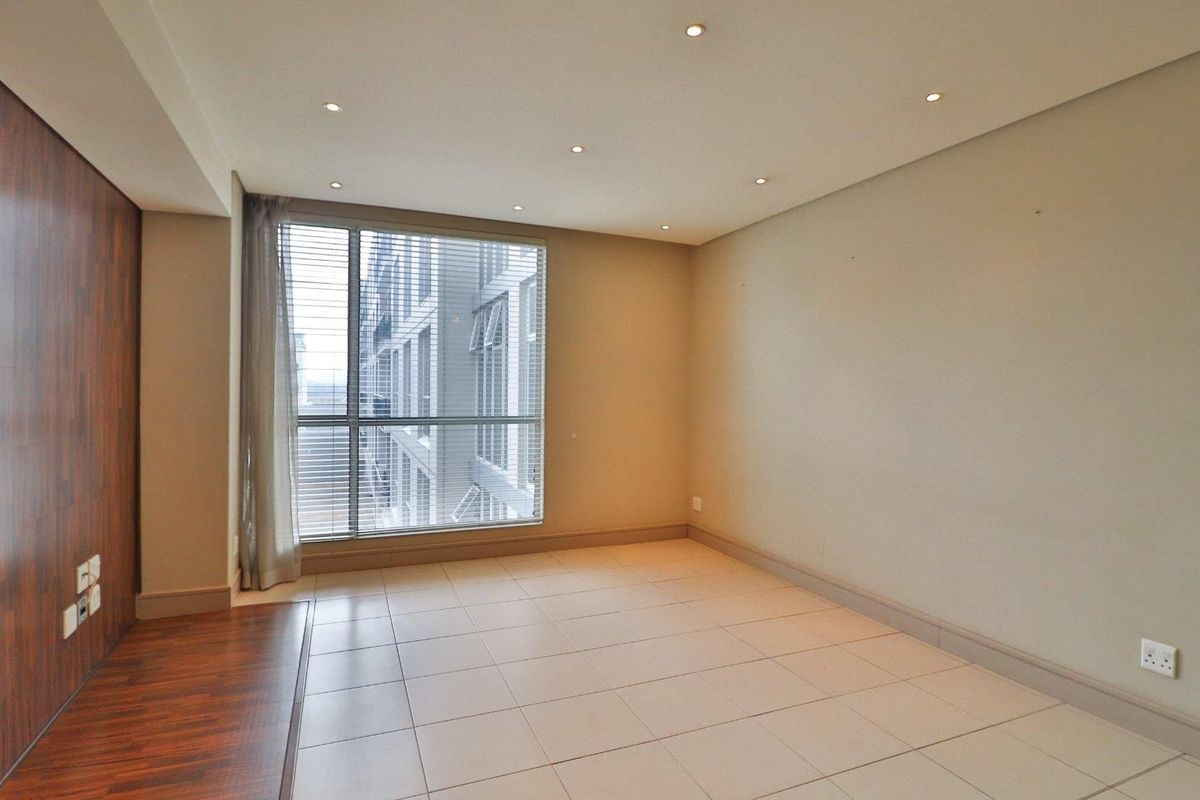 A bright, empty living area featuring tiled floors, recessed downlighting, and a modern wood-look feature wall with large windows providing natural light.