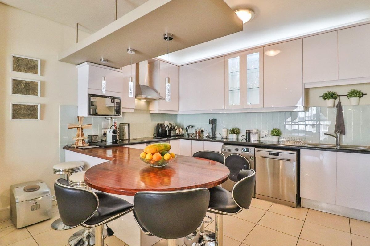 Modern kitchen featuring high-gloss cabinetry, a built-in microwave, integrated extractor fan, tiled backsplash, and a functional breakfast bar with pendant lighting.