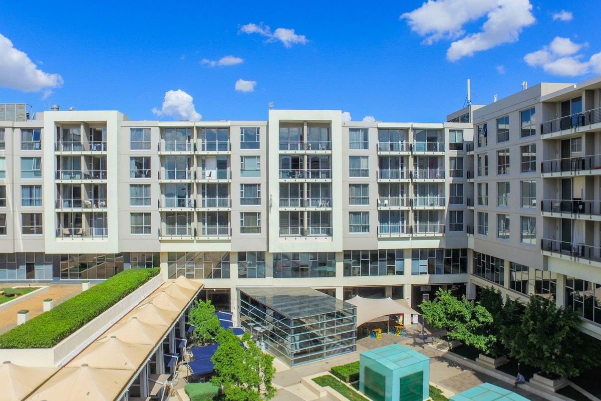 An aerial view of a modern apartment complex featuring a central landscaped courtyard, glass atrium, and multiple levels of private balconies.