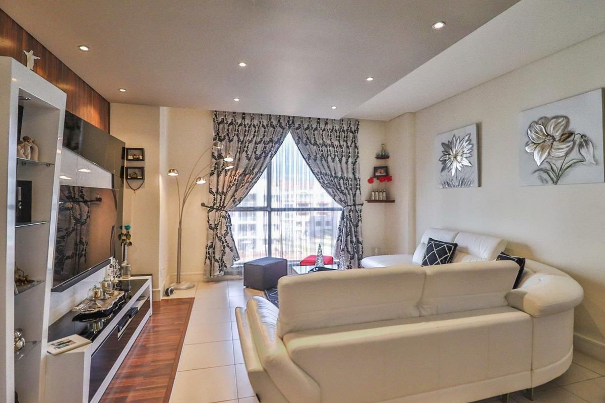 A well-maintained living room featuring a combination of tiled and laminate flooring, recessed lighting, and a custom built-in media wall unit.