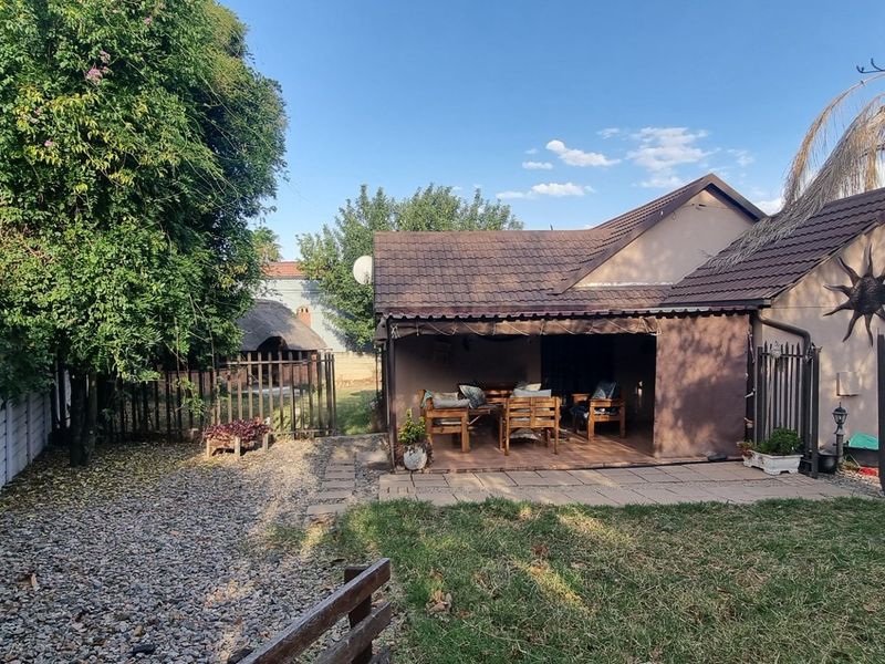Rear view of the property featuring a covered patio, paved outdoor space, gravel garden area, and perimeter security fencing.