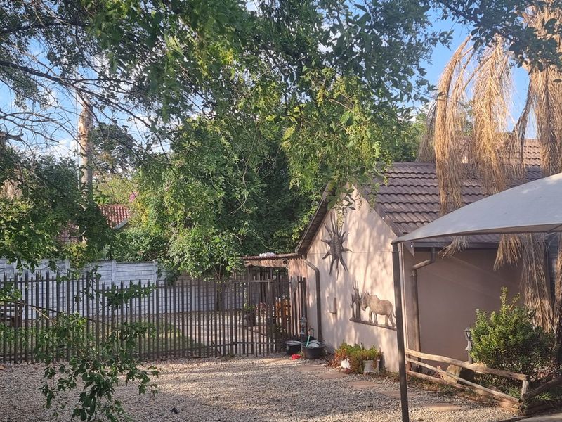 A view of the rear exterior area featuring a tiled roof structure, gravel ground cover, and metal perimeter fencing with a shade sail.